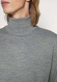 Grå turtleneck genser laget av myk, strukturert strikket stoff, med høy krage og tettsittende design som fremhever en jevn overflate.