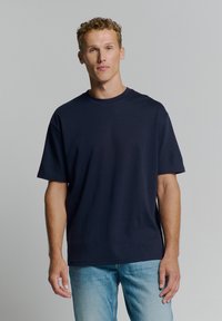 Navyblauwe oversized t-shirt met een ronde hals, korte mouwen en een soepele textuur. Gepaard met lichtblauwe denim jeans.
