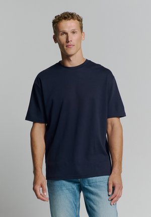 Navy blue oversized t-shirt with a crew neck, short sleeves, and a smooth texture. Paired with light blue denim jeans.
