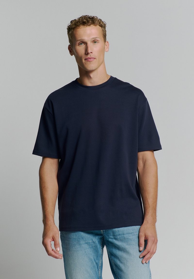 Navyblauwe oversized t-shirt met een ronde hals, korte mouwen en een soepele textuur. Gepaard met lichtblauwe denim jeans.