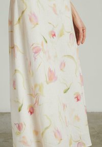 Kleid mit Blumenmuster, das einen weißen Hintergrund mit sanften rosa Tulpen und grünen Stielen zeigt. Der Stoff wirkt leicht und atmungsaktiv.