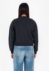 Felpa nera con colletto rotondo e maniche raglan, abbinata a jeans in denim blu a vita alta. Tessuto morbido, vestibilità rilassata.