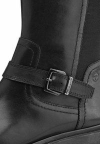 Bota de cuero negra con panel lateral sintético, correa con hebilla de metal y detalles de costura. Textura suave y diseño de puntera redondeada.