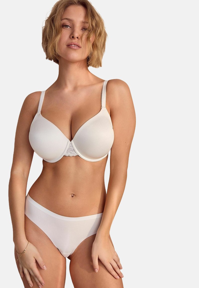 Soutien-gorge blanc avec des coques lisses et des détails en dentelle sur la bande, associé à un slip blanc uni. Les deux sont fabriqués en tissu doux et extensible.