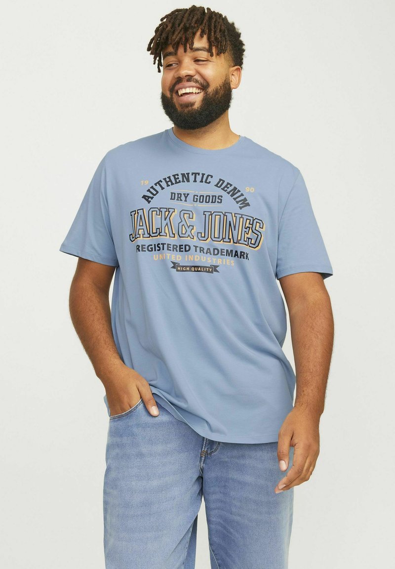 Camiseta de manga corta azul claro con texto en negro y dorado: "DENIM AUTÉNTICO JACK & JONES," combinada con unos vaqueros azul claro.