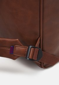 Borsa in pelle sintetica marrone con superficie texturizzata. Presenta una fibbia scura e una tracolla intrecciata, con dettagli di cucitura lungo i bordi.