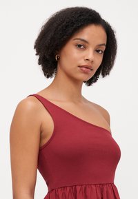 Vestido burdeos de un solo hombro con textura acanalada, corsé ajustado y falda de vuelo. Tejido suave, diseño minimalista, sin estampados ni herrajes.