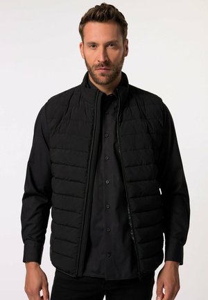 Black padded vest with a high collar, zip closure, and horizontal quilting pattern, worn over a black button-up shirt. Smooth texture.