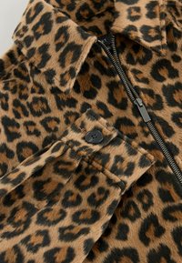 Leopardmønstret uldfrakke med krave, synlig sort knap på manchetten og sølv lynlås delvist lukket.