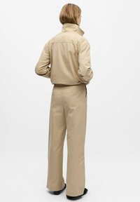 Beige katoenen shirt en wijde broek, met een hoge kraag, een relaxte pasvorm en zijsplitten, weergegeven tegen een effen witte achtergrond.