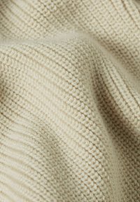 Natuurlijk beige gebreide stof met een textuur en een geribbelpatroon met verschillende steken, dat de zachtheid en warmte benadrukt.