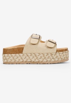 Beżowa sandałka na platformie z dwoma regulowanymi paskami z klamrami i plecioną jutyową podeszwą na jednolitym białym tle.