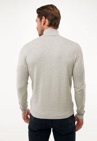 Jasnoszary sweter z wysokim kołnierzem, prążkowanymi mankietami i dołem. Ma gładką strukturę i dopasowany krój, noszony na ciemnych dżinsach.