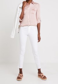 Ljusrosa, kortärmad skjorta med knäppning och två bröstfickor, ihop med vita tajta jeans och rosa platåsandaler. Vit denimjacka hängande över axeln.