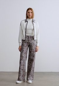 Λευκό μπουφάν με φερμουάρ συνδυασμένο με παντελόνι λεοπάρ. Υφή υφάσματος, μακριά μανίκια, ψηλός γιακάς, άνετη εφαρμογή και φαρδιά γραμμή παντελονιού. Λευκά αθλητικά παπούτσια ολοκληρώνουν την εμφάνιση.