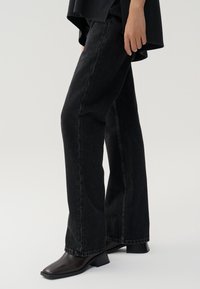 Black wide-leg jeans made from denim, featuring a high waist, straight legs, and subtle fading, paired with dark brown ankle boots.