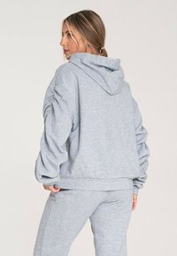 Szara bluza z kapturem, marszczonymi rękawami i skróconym fasonem. Wykonana z miękkiego materiału, w połączeniu z dopasowanymi szarymi spodniami dresowymi.