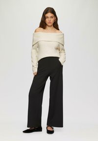 Crème ribbed off-shoulder trui gecombineerd met zwarte wijde broek, aangevuld met zwarte platte schoenen. Eenvoudig ontwerp met strakke lijnen.