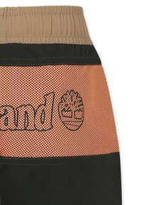 Pantaloni corti con cintura elastica, parte superiore in rete arancione traspirante, sezione inferiore nera e logo Timberland stampato in nero.