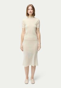 Virkat tröja och utsvängd kjolset i ljus beige. Texturerad tyg med korta ärmar, rund hals och en figurnära, sömlös design.