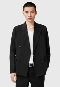 Blazer doppiopetto nero realizzato in tessuto morbido, caratterizzato da due tasche frontali, rever con scollatura a poncho e chiusura con bottoni decorati.