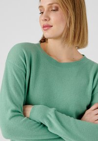 Suéter verde menta hecho de un tejido suave y texturizado, con cuello redondo y mangas largas. Diseño simple sin patrones o acentos visibles.
