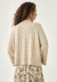 Suéter de punto beige con cuello y dobladillo acanalados. Textura suave, longitud corta, combinado con una falda de estampado floral.
