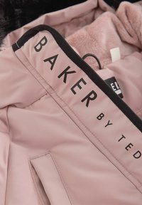 Fuchsia jakkeinteriør med blødt, pelsagtigt for. Har et sort mærke med teksten "BAKER by TED" i fed skrift. Glat materiale, ingen synlige mønstre.