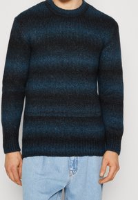Maglione a righe blu scuro e nero in maglia con texture a coste, scollo rotondo e maniche lunghe. Presenta una vestibilità comoda e un design informale.
