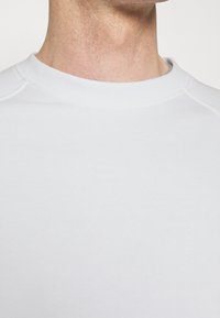 Sudadera de cuello redondo color gris claro, confeccionada en tela suave, con puños y cuello acanalados. Textura lisa sin patrones ni detalles visibles.