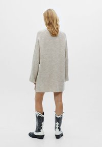 Pull en maille essentiel beige oversize à manches longues, associé à des bottes de cowboy noir et blanc ornées de coutures élaborées et à un talon bas.
