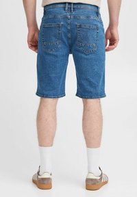 Denim šorti vidēji zilā krāsā, ar taisnu piegriezumu, aizmugurējām kabatām ar izšūtu akcentu un neapstrādātu apdari. Valkāti ar pelēkbrūniem apaviem.