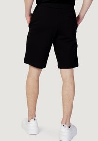 Pantaloni corti neri di cotone con elastico in vita, vestibilità rilassata, tasche laterali e texture liscia, abbinati a scarpe da ginnastica bianche.