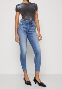 Jeans de denim azul ajustados con una cintura de altura media, combinados con una camiseta negra ajustada y brillante, y tacones negros de punta.