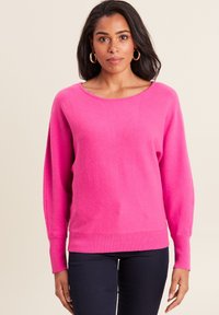 Felroze trui met een brede halslijn en lange, licht gepofte mouwen. Ribbelboord aan de onderkant en bij de mouwen. Zachte textuur. Gecombineerd met donkere pantalons.