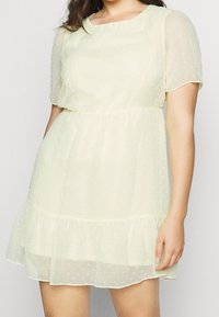 Abito a maniche corte, lungo fino al ginocchio, realizzato in tessuto giallo leggero e testurizzato con pois bianchi e orlo arricciato. Collo rotondo.