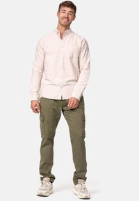 Camisa de botones de manga larga color rosa claro con bolsillo, combinada con pantalones cargo verde oliva y zapatillas color beige. Ajuste casual y diseño relajado.