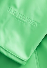 Tejido impermeable verde con el nombre de la marca "ILSE JACOBSEN" en relieve, textura suave y un sutil brillo, con costuras destacadas en los bordes.