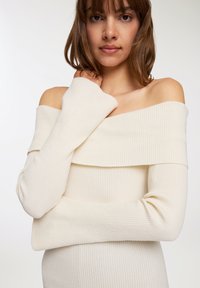 Maglione crema off-shoulder con texture a coste, maniche lunghe e design a strati. Tessuto a maglia morbido, silhouette attillata.