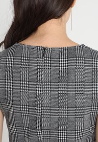 Robe à carreaux noir et blanc avec un col rond, des manches courtes et une fermeture éclair dans le dos. Tissu lisse avec un motif texturé.