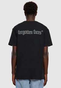 Černé bavlněné tričko s nápisem "zapomenuté tváře" v bílé, texturované grafice na zádech, krátkými rukávy a volným střihem.