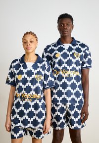 Marinblå och vit mönstrad träningskläder med geometrisk design. Inkluderar shorts och matchande kortärmade polo tröjor med logotypdetaljer.