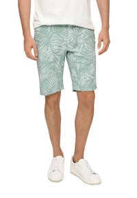 Pantaloni corti verde chiaro con un motivo di foglie tropicali bianche, realizzati in tessuto leggero, abbinati a sneakers bianche. Taglio dritto, lunghezza sopra il ginocchio.