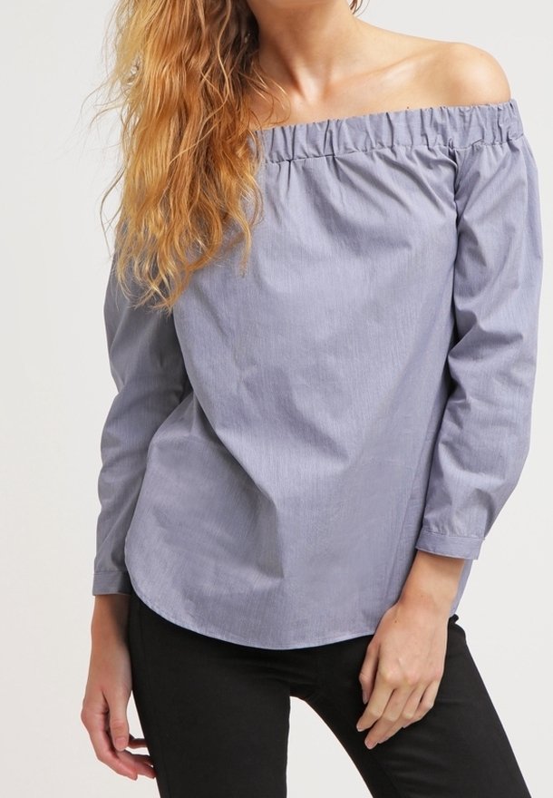 Halenka bez ramínek, světle modrá s pruhy, dlouhé rukávy, nařasený výstřih a volný střih, nošena s černými kalhotami.