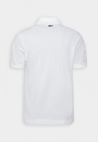 Polo shirt blanc à manches courtes, doté d'un col classique et d'un petit logo crocodile vert dans le haut du dos. Texture douce.