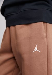 Brown sweatpants featuring a white Jumpman logo, made of soft material with a relaxed fit and elastic waistband, paired with a black top.