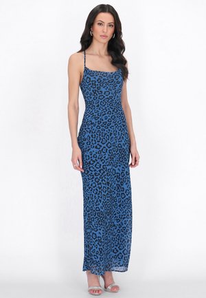 Kvinde i en blå kjole, der går til anklerne, med sorte leopardpletter og tynde stropper, iført sølvfarvede åbne hæle.