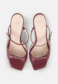 O pereche de sandale din piele burgundă, cu vârf deschis, curea la glezna și față pătrată, pe un fundal deschis.