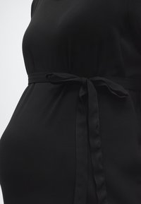 Primer plano de un vestido de maternidad negro con un cinturón de tela atado sobre una barriga embarazada.