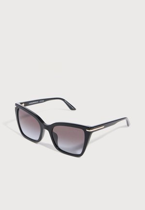 Black oversized square sunglasses with gradient dark lenses and thin gold accents on the temples, displayed on a white surface.